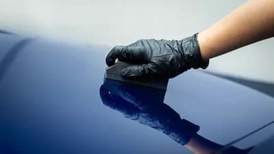 Gloved hand applying ceramic coating on a blue car surface